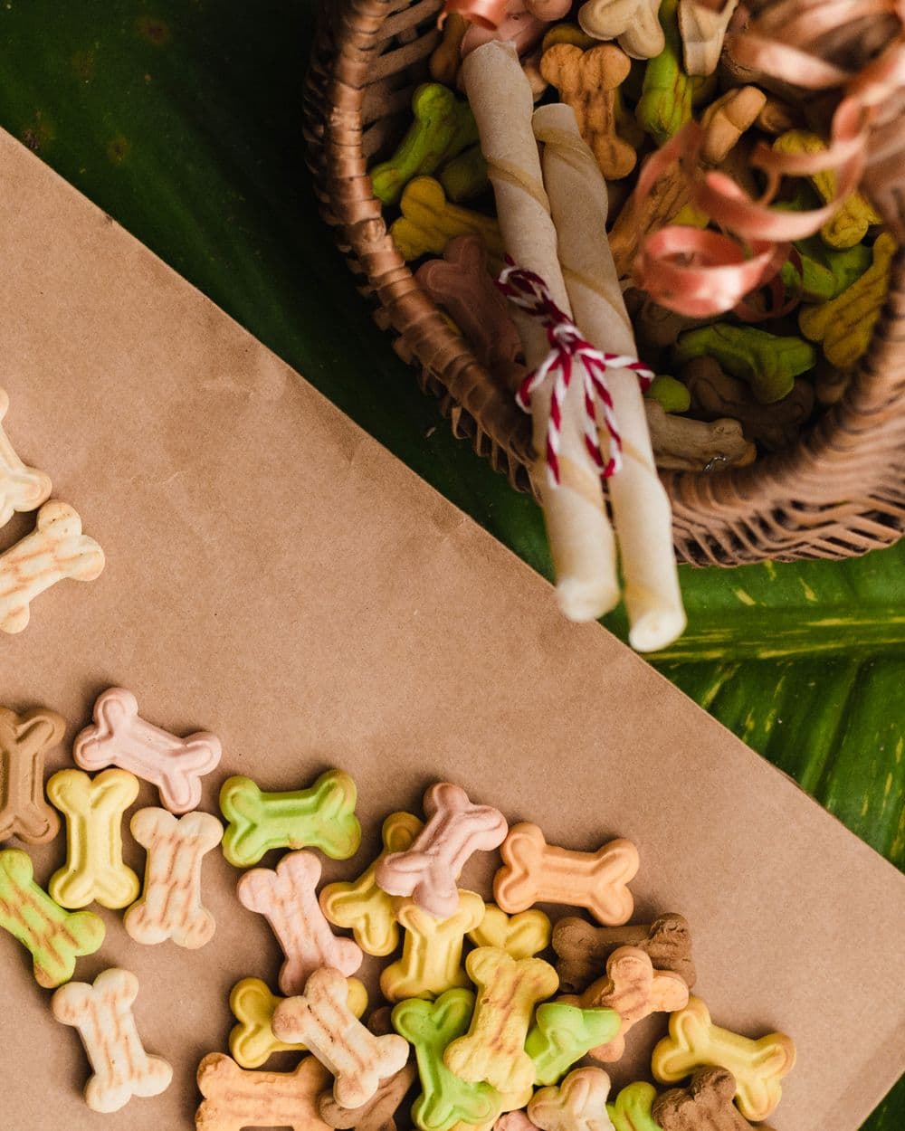 Assorted bone-shaped dog treats and rolled chews in a woven basket