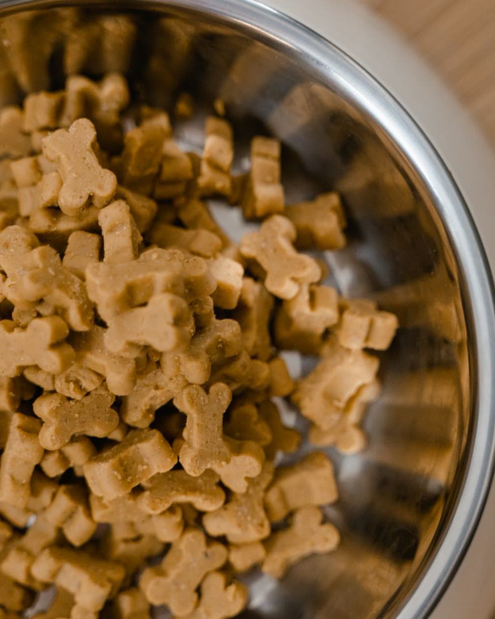 Bone-shaped baked dog biscuits filling a stainless steel bowl